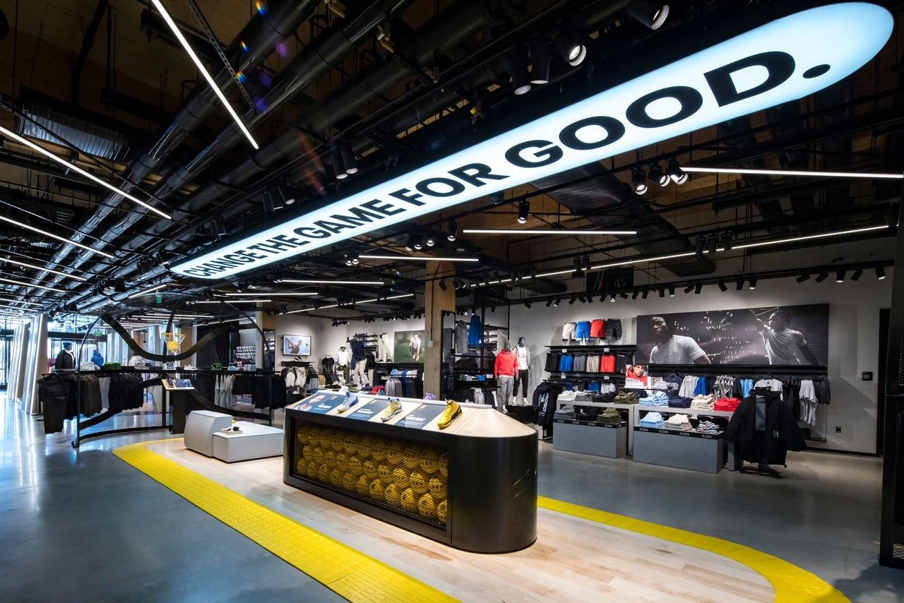 Under Armour: Store interior with a curved overhead sign, a central display table and yellow floor lines
