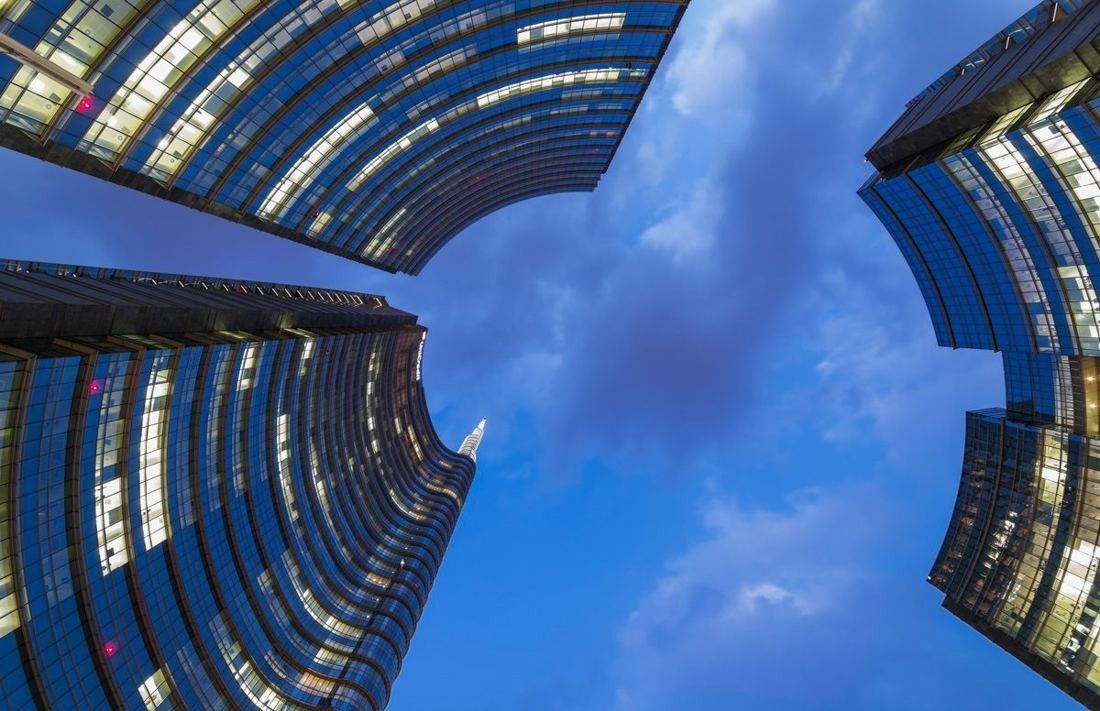 UniCredit: Looking up between curved glass towers toward a blue sky with clouds
