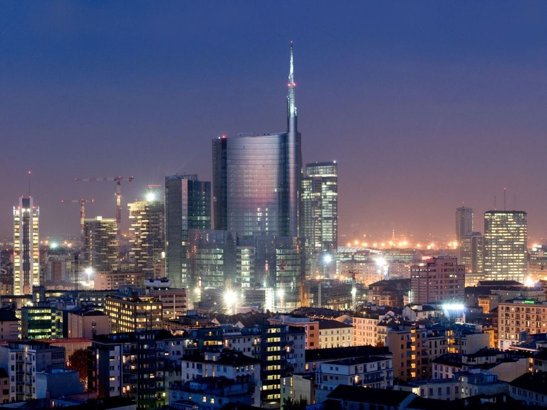 UniCredit: Night skyline with the spired tower among lit high-rises above city roofs
