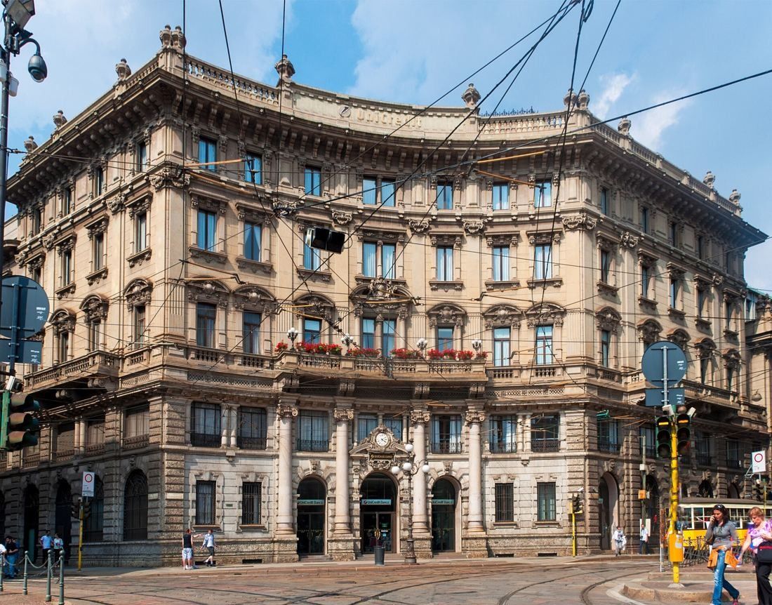 Ornate stone palazzo with a curved facade on a city square with tram wires
