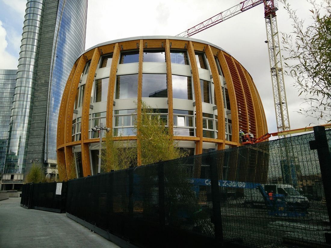 UniCredit: Oval building with curved timber ribs and glass, behind a fence near glass towers