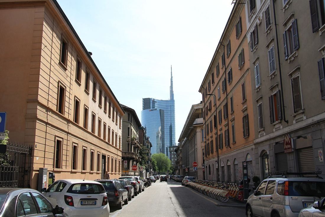 UniCredit: Street lined with older buildings and parked cars leading to the spired tower