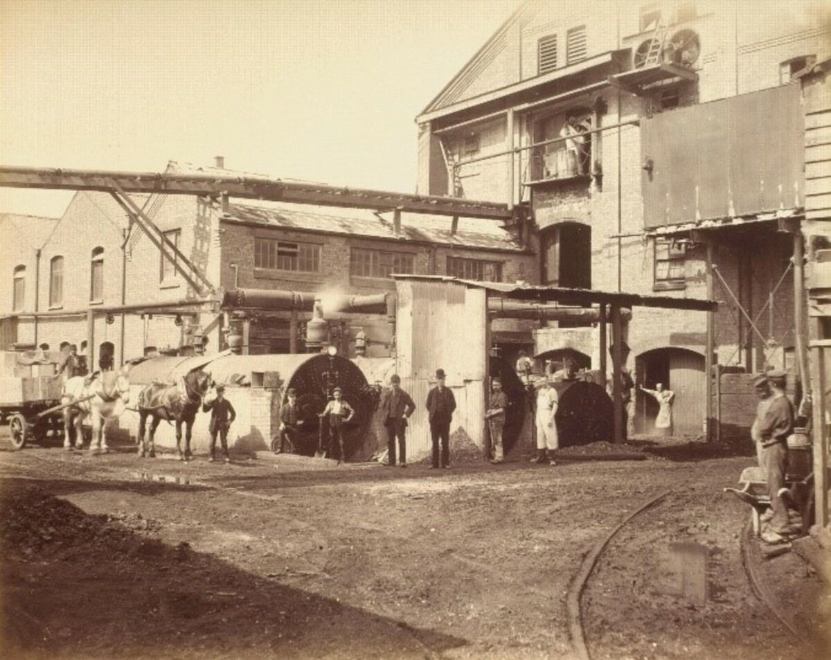 Sepia photo of a soap works yard with horse-drawn carts in front of brick factory buildings