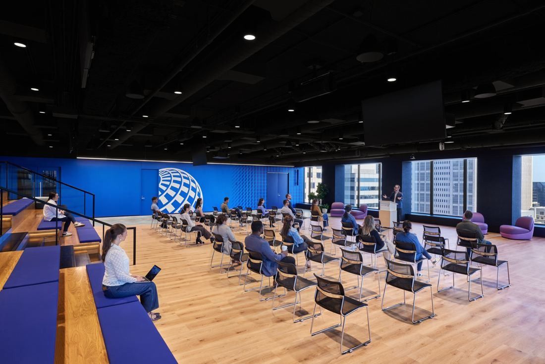 United Airlines: Large room with rows of chairs, a wood floor and blue bench seating along the side
