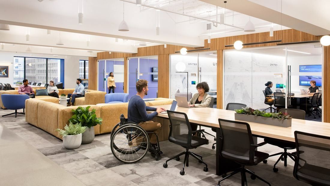 United Airlines: Open workspace with long tables, sofas and plants beside glass meeting rooms