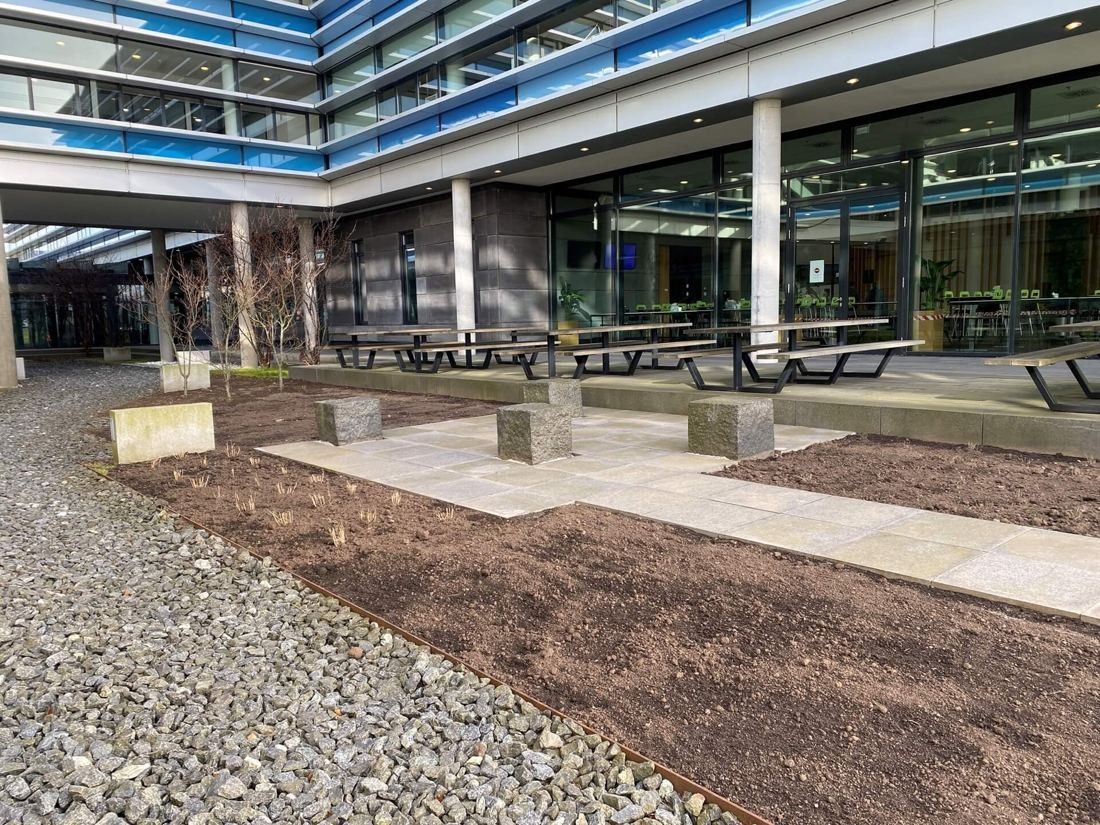 Vestas: Courtyard beds of soil and gravel with stone blocks and picnic tables before a glass façade