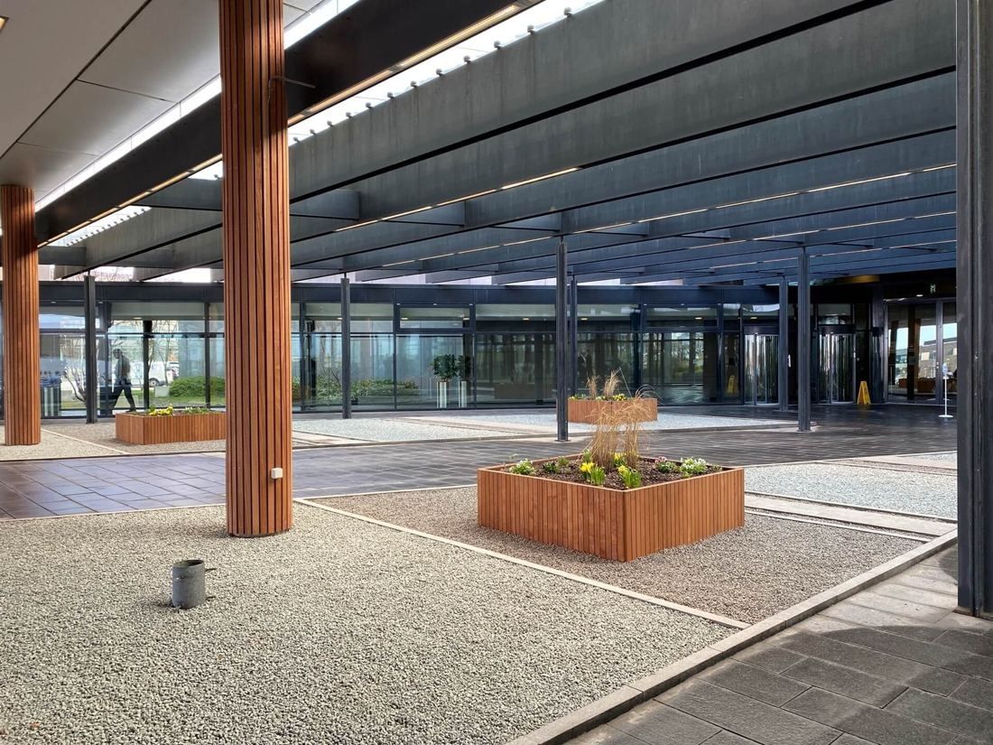 Vestas: Covered entrance area with wooden columns, a gravel bed and a wooden planter in front of glass doors
