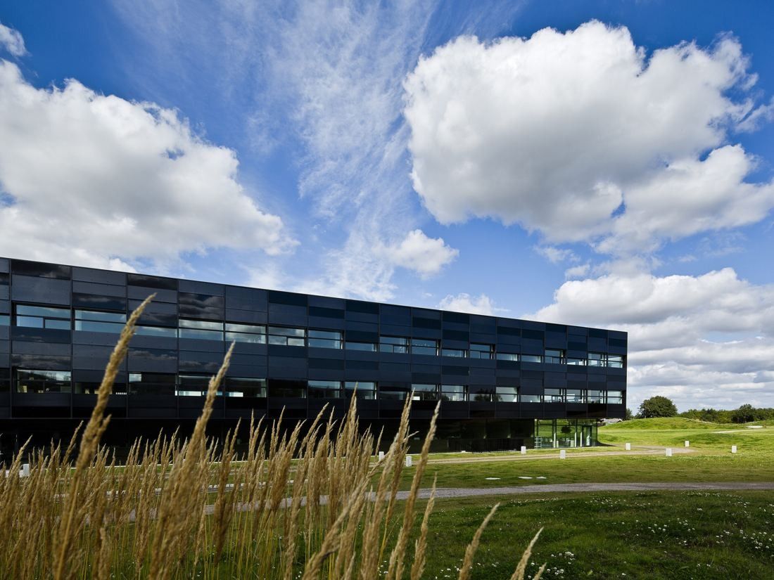 Vestas: Dark glass office building behind tall grasses with large white clouds above