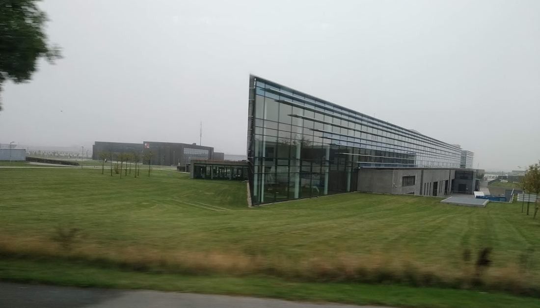 Vestas: Glass building with an angled roofline seen across a wide lawn on an overcast day