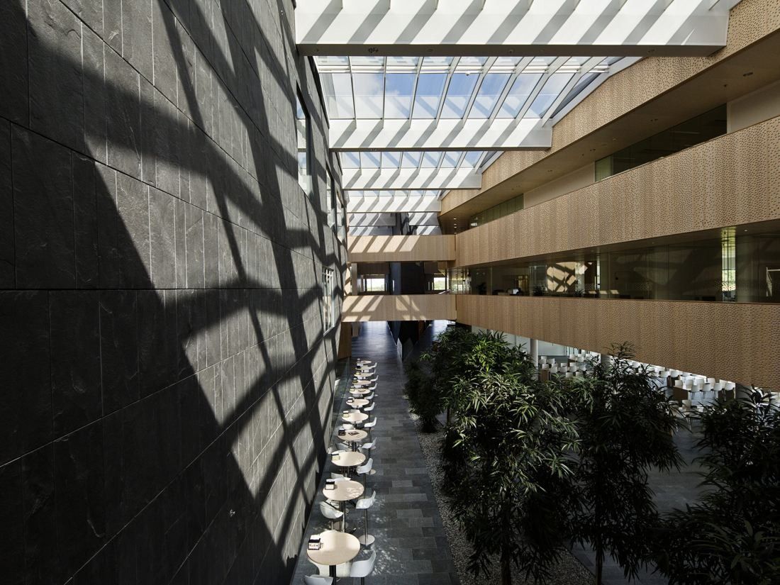 Vestas: Glass-roofed atrium with wooden balconies on one side, a dark tiled wall on the other and trees and tables below