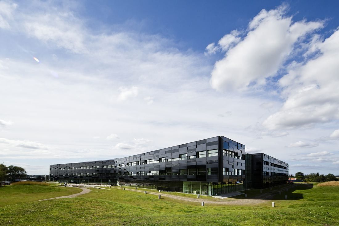 Vestas: Long low dark office building seen across grass mounds and a curving path