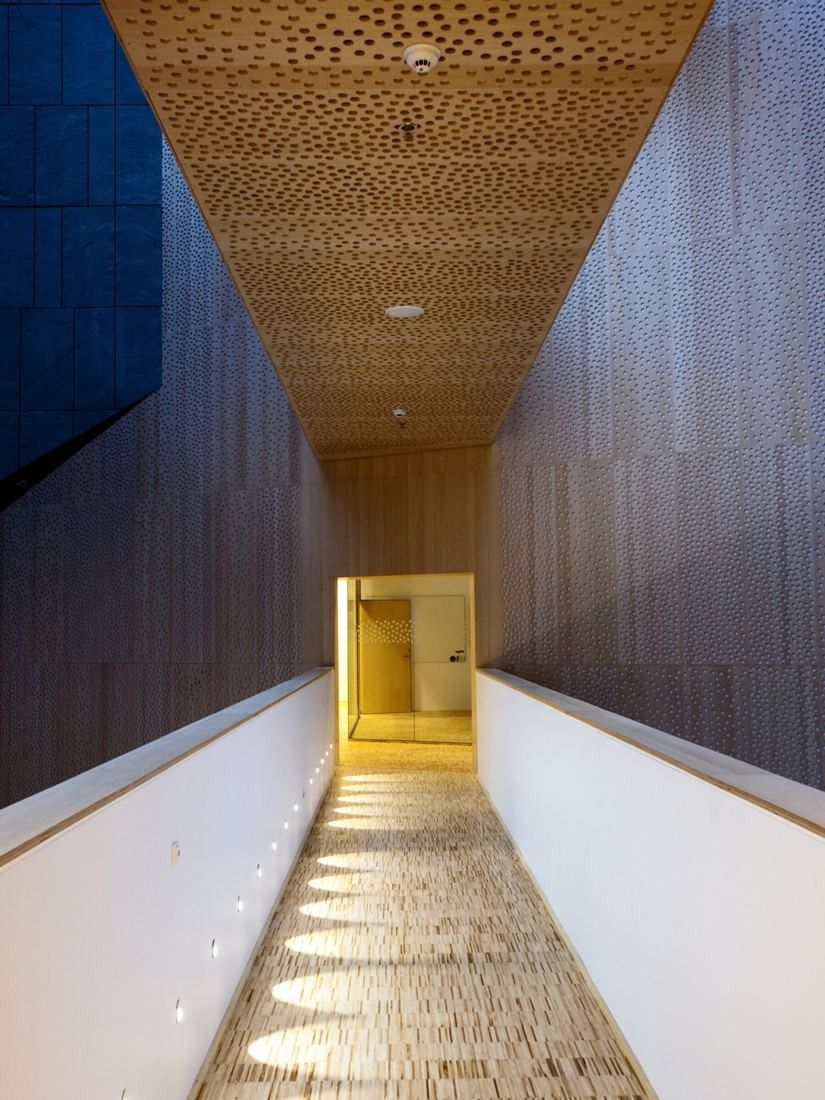 Vestas: Narrow corridor with dark wood walls and a perforated wooden ceiling leading to a lit opening