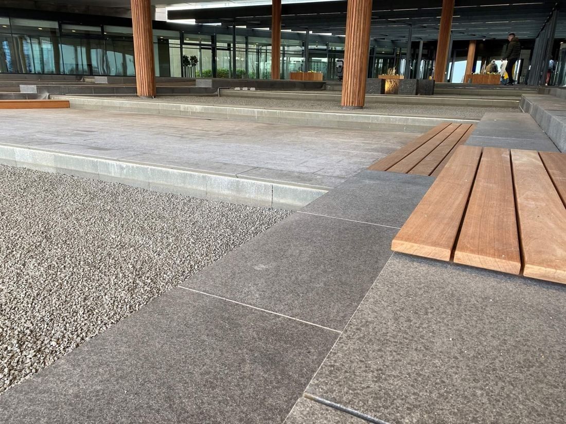 Vestas: Wooden bench on stone paving beside gravel, with wooden columns behind