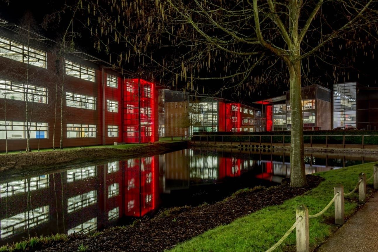 Vodafone: Office buildings with red-lit stair towers reflected in a pond at night