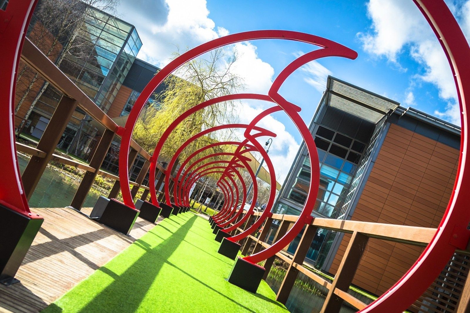 Vodafone: Red looping sculpture arching over a grass path between office buildings