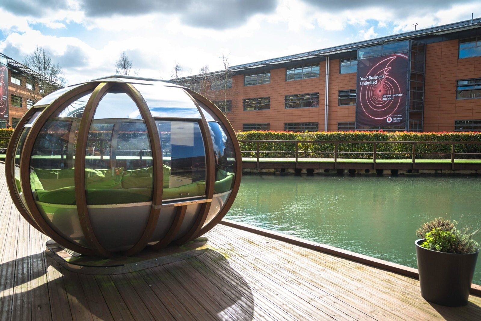 Vodafone: Round wooden-framed glass pod on a deck beside the lake, office building behind