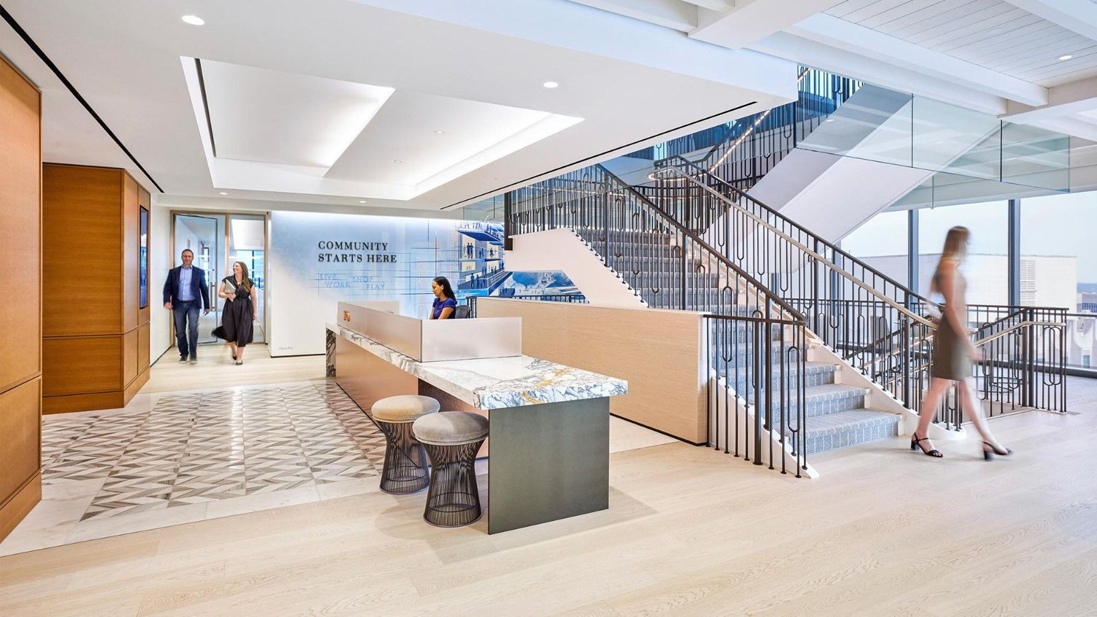 A bright entrance with a marble reception desk and a wooden stair with a carpet runner