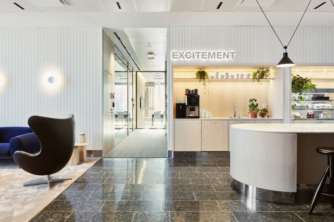 Wärtsilä: Lobby with a dark stone floor, a black egg chair, a curved white counter and a coffee bar under the word EXCITEMENT