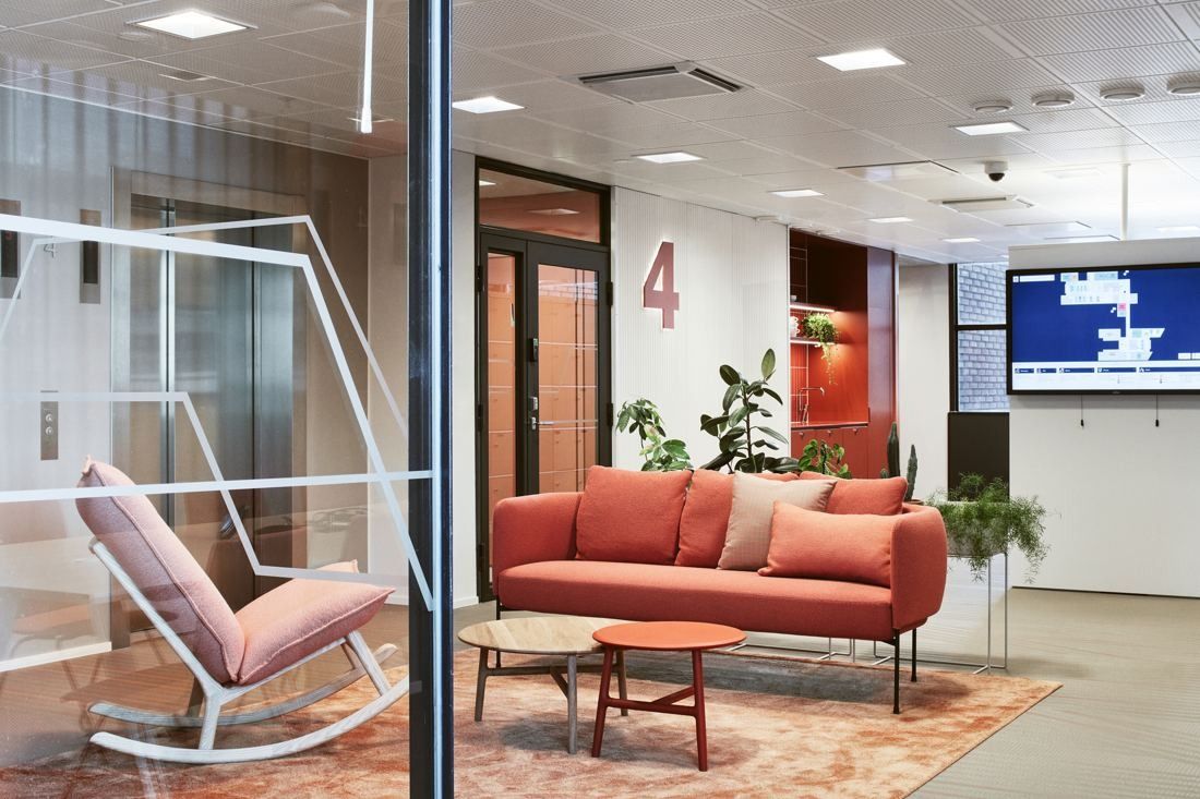 Wärtsilä: Lounge corner with a coral sofa, a rocking chair and a round coffee table near a lift lobby marked 4