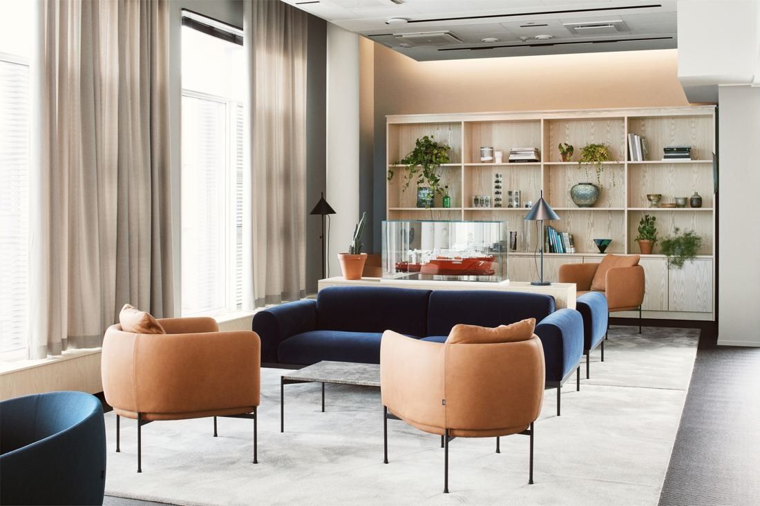 Wärtsilä: Lounge with tan armchairs, a navy sofa and open shelving beneath tall curtained windows