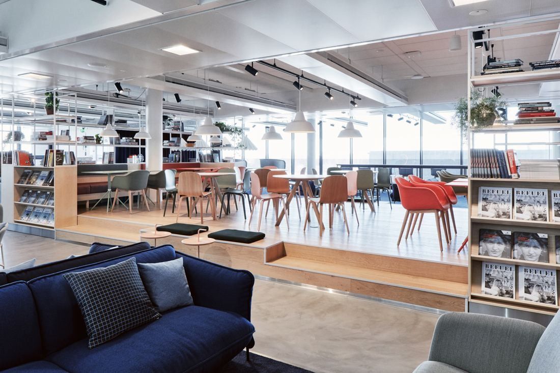 Wärtsilä: Open office floor with sofas, bookshelves and red chairs under track lighting, windows along the far side