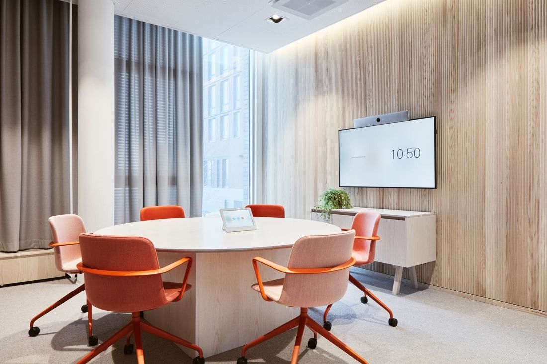 Wärtsilä: Round white table with orange chairs and a wall screen in a room lined with pale wood