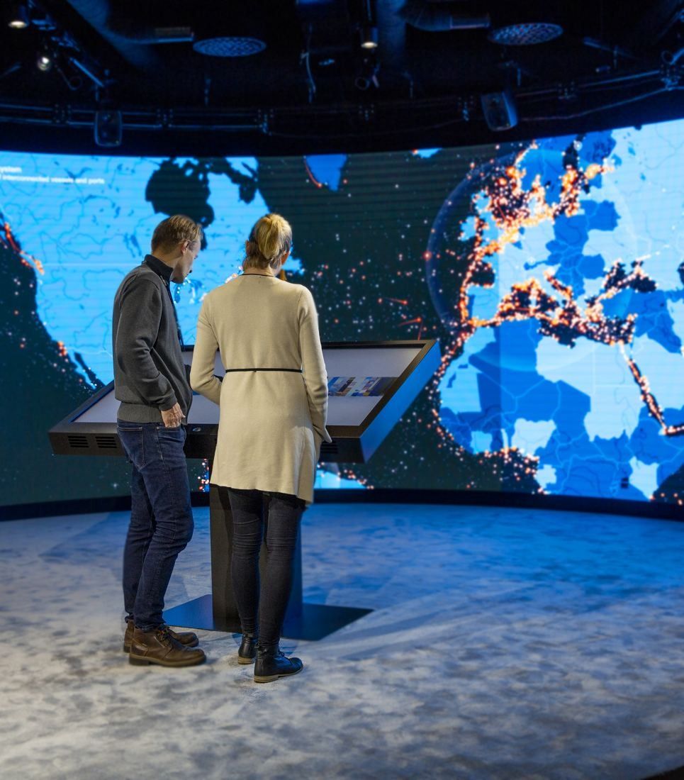 Wärtsilä: Two people seen from behind standing before a curved screen showing a glowing world map