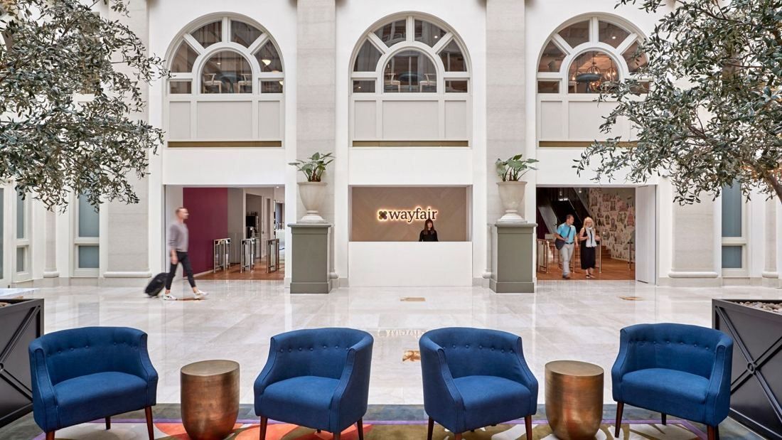 Wayfair: Bright reception hall with arched windows, white columns, potted trees and a row of blue armchairs