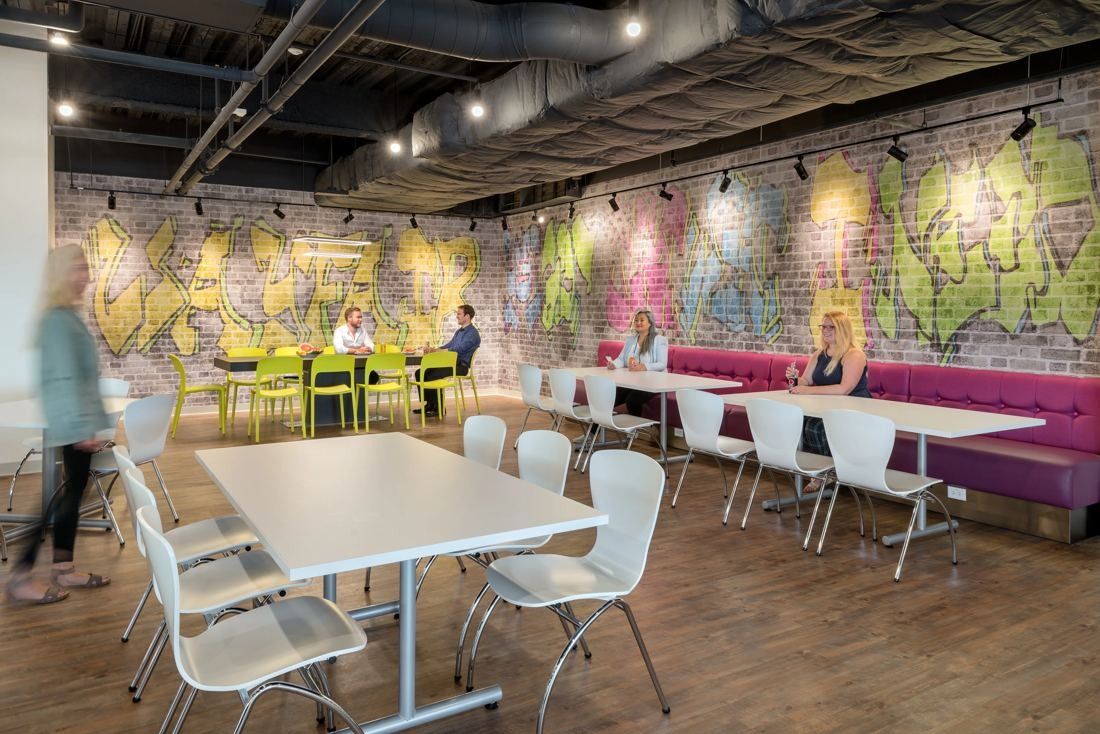 Wayfair: Dining area with white tables and chairs, a magenta banquette and a graffiti-painted brick wall