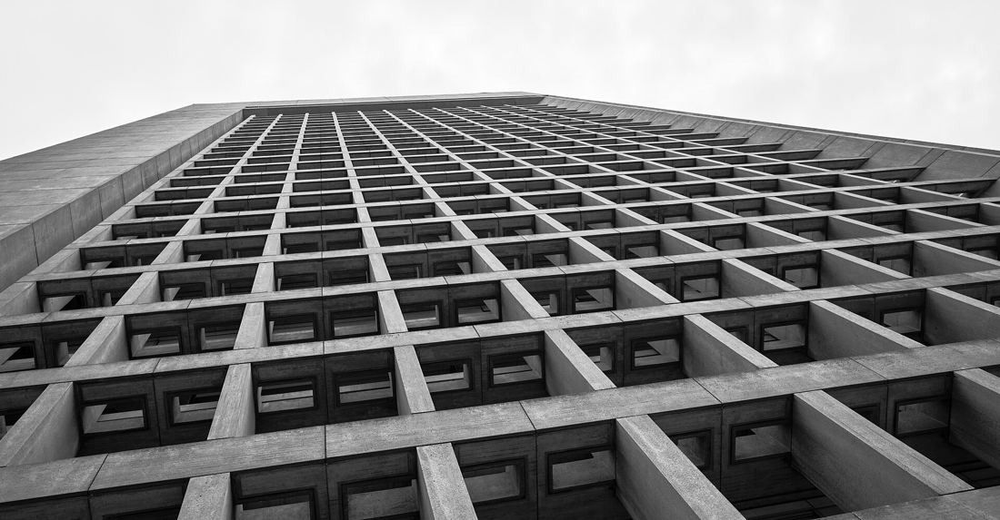 Grid of deep concrete window frames on a high-rise facade seen from below