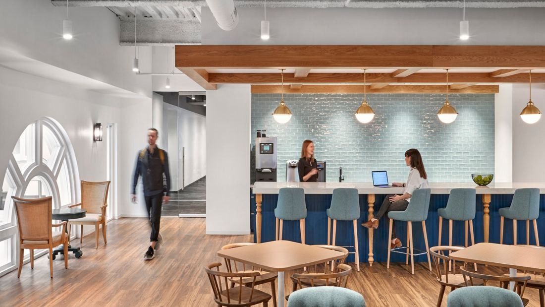 Wayfair: Kitchen bar counter with blue stools, brass pendant lights and wooden tables beside an arched window
