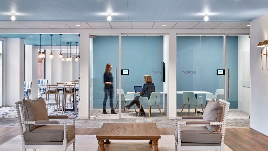 Wayfair: Lounge chairs around a wooden coffee table in front of glass-walled meeting rooms