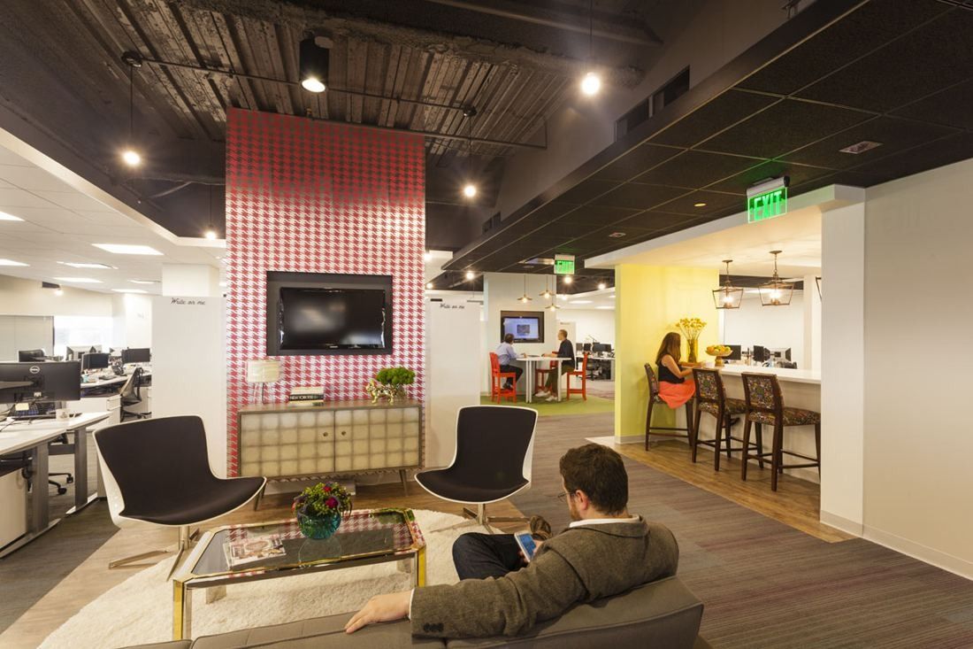 Wayfair: Lounge corner with black chairs and a houndstooth-patterned wall, beside open desks and a yellow bar nook