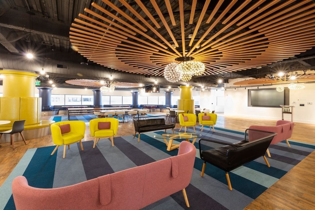 Open lounge with a radial wooden slat ceiling, globe pendant lights, pink and yellow sofas and armchairs on striped rugs