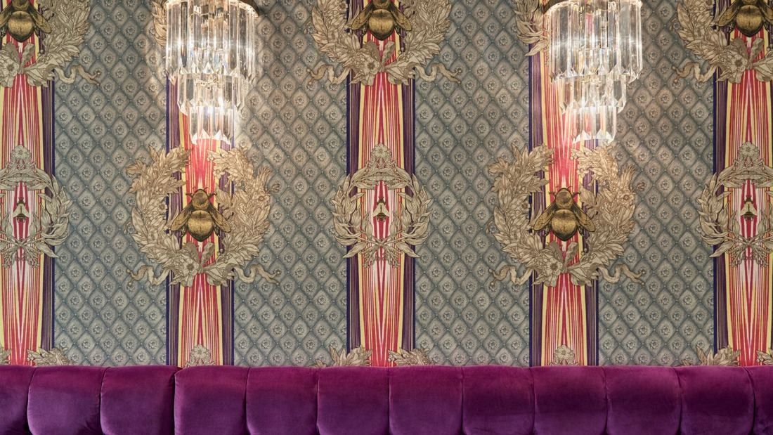 Wayfair: Purple velvet banquette below ornate patterned wallpaper and crystal chandeliers