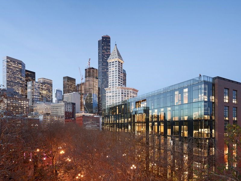 Glass and brick office building above trees at dusk with skyscrapers behind