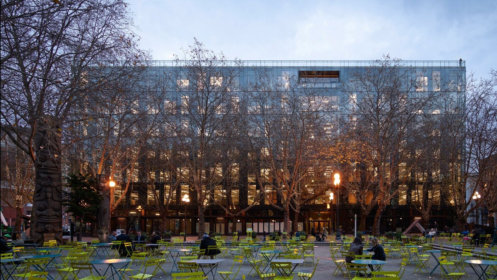 Weyerhaeuser: Glass building behind bare trees and park tables at dusk