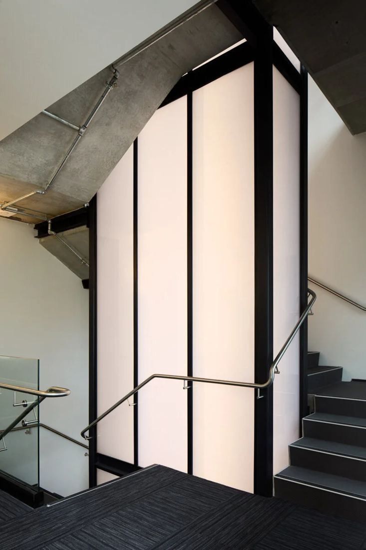 Xero: Concrete stair winding around a backlit white panel