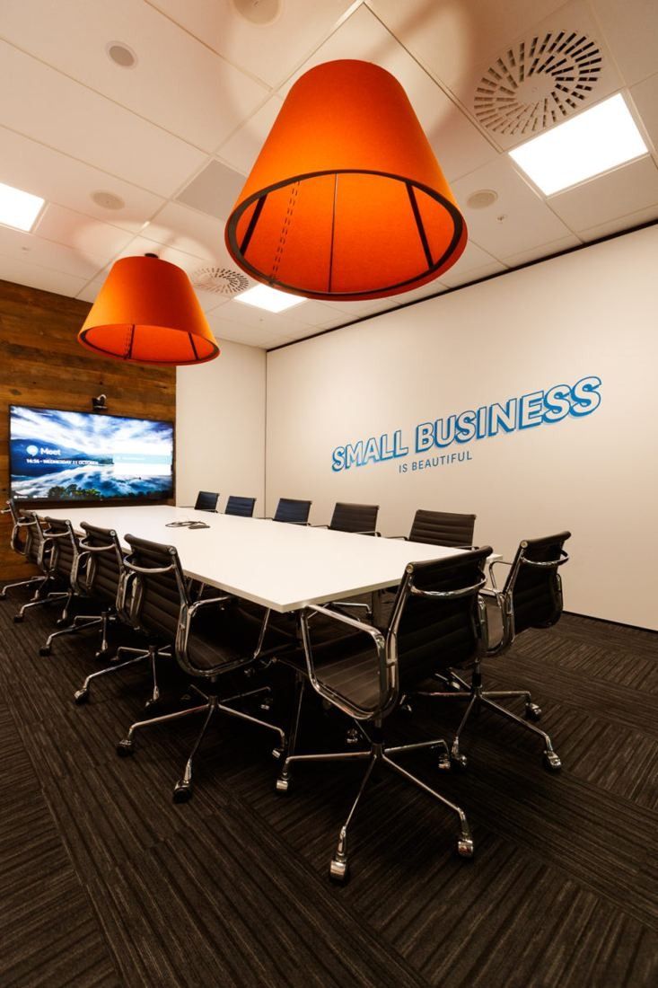 Xero: Meeting room with a long white table, black chairs, a wall screen and orange pendant lamps