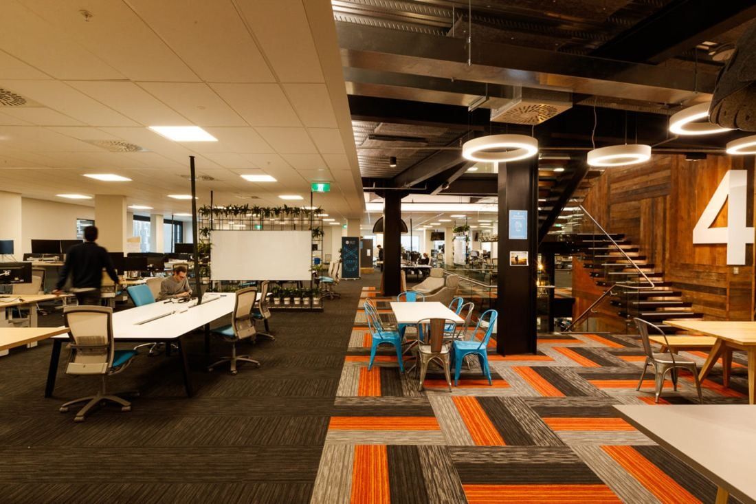Xero: Open office floor with long white desks, orange and grey patterned carpet and a timber-clad stair marked 4