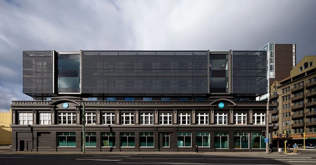 Xero: Street-front view of a long heritage facade with arched windows, topped by dark upper floors behind a mesh screen