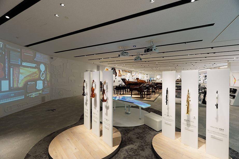 Yamaha: A dim exhibition hall with instruments on white stands and a grand piano in the background
