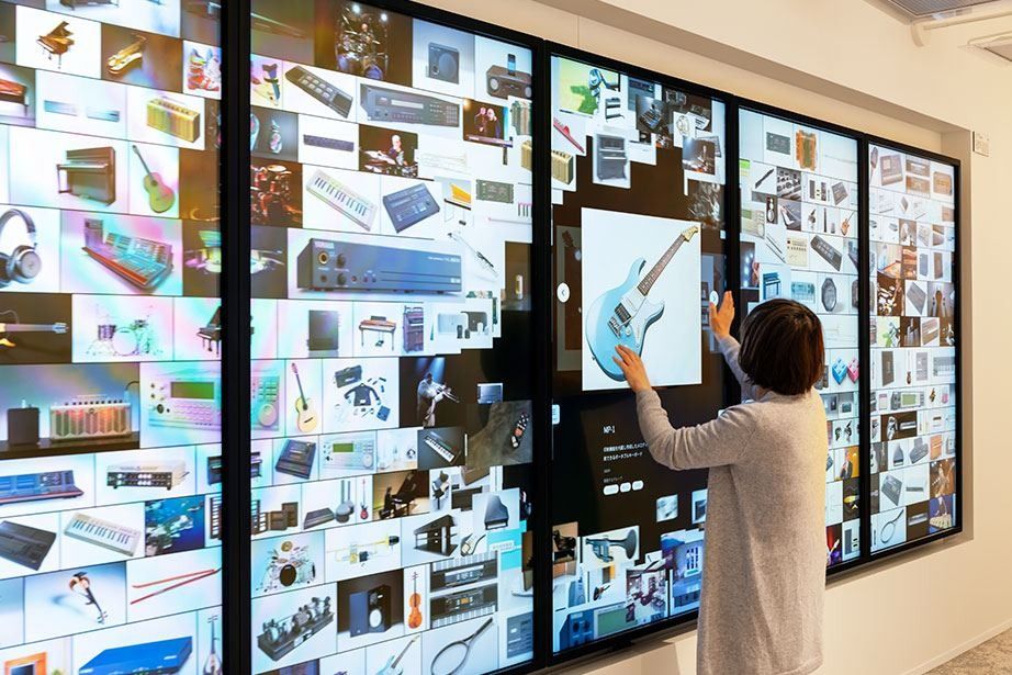 Yamaha: A large interactive display wall of product images, with a visitor seen from behind touching the screen