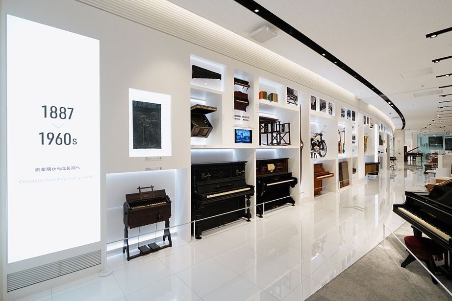 Yamaha: A long white museum gallery with pianos and instruments displayed along a curving wall