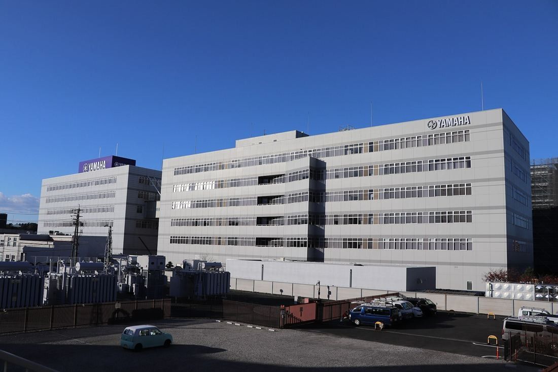 Yamaha: Large white multi-story office buildings behind a parking lot under a deep blue sky
