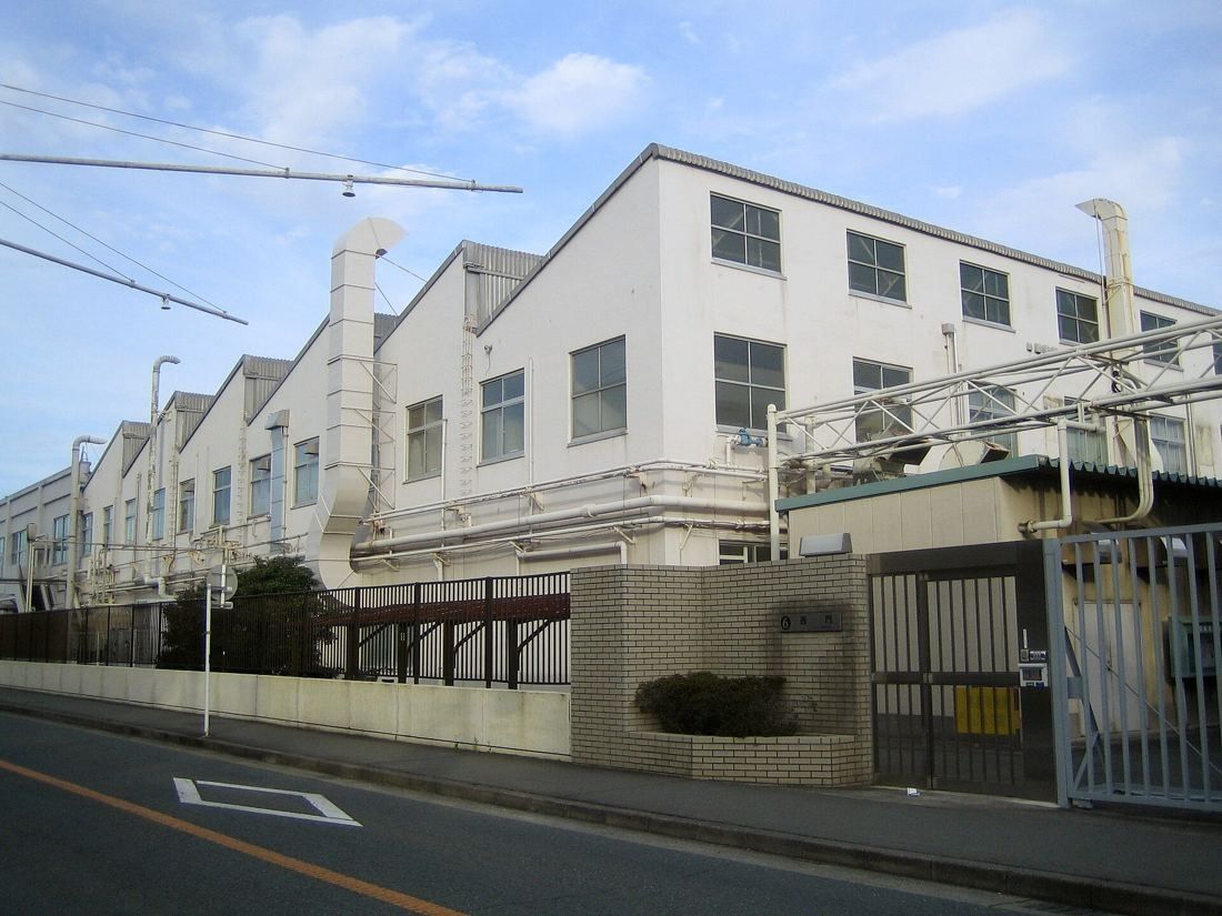 Yamaha: White factory buildings with sawtooth roofs, ducts and a gate along a street