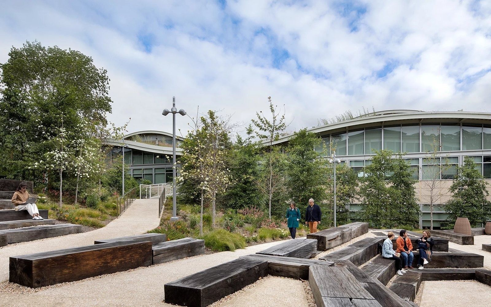 YouTube: Courtyard with heavy timber benches on gravel in front of curved-roof buildings