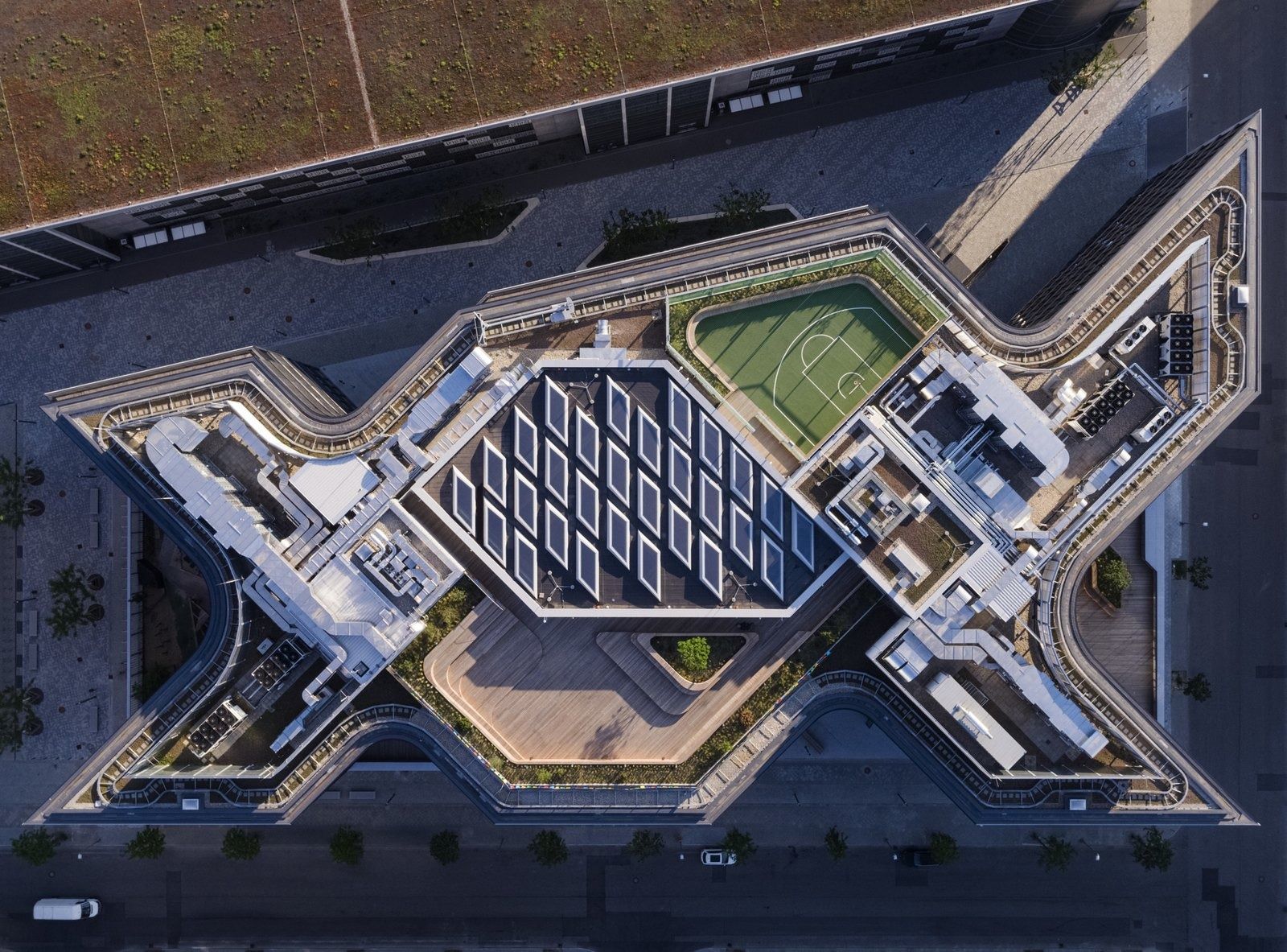 Zalando: Aerial view of a building with a zigzag plan, glass roof over the atrium and a green rooftop court