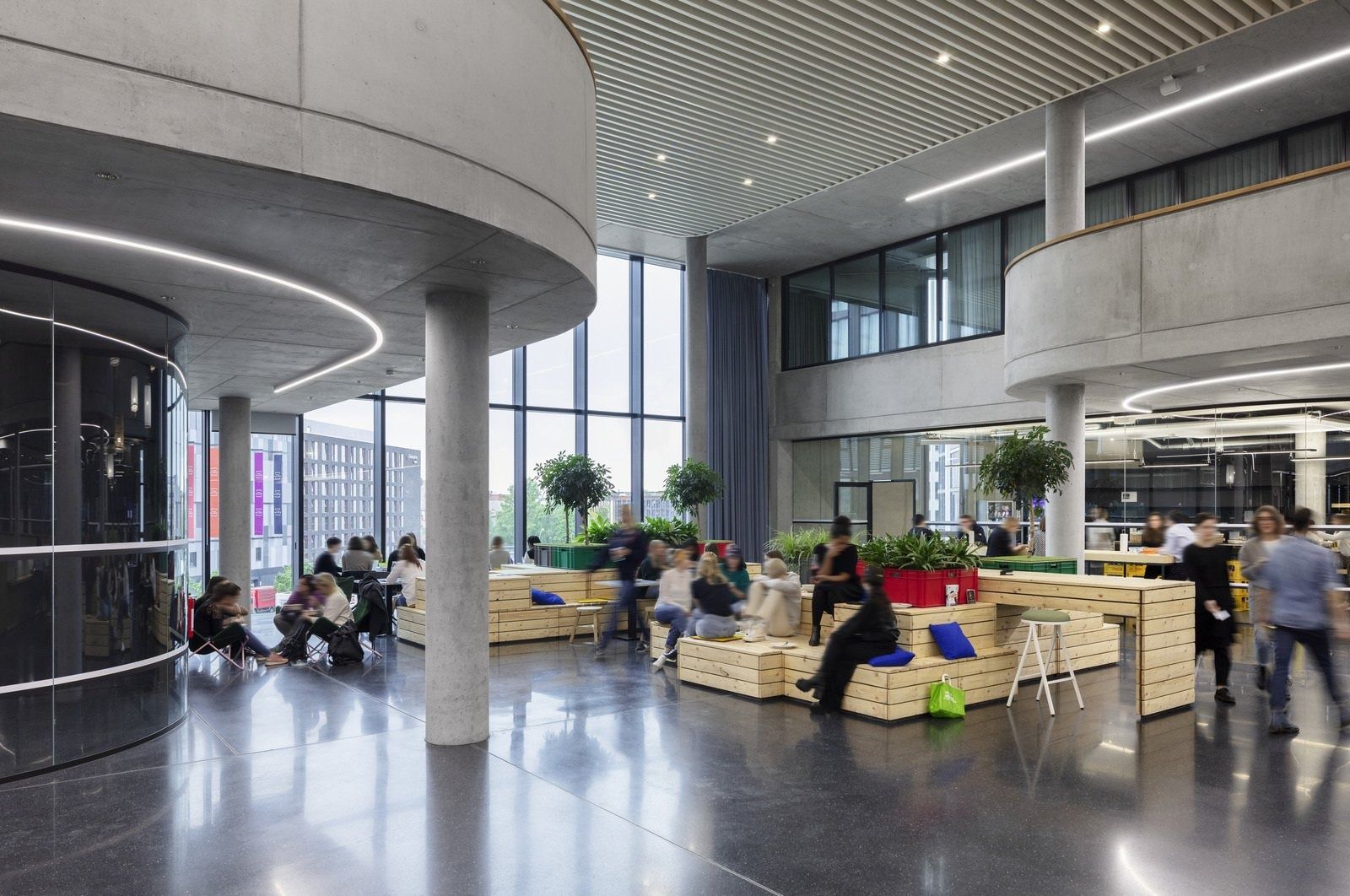 Zalando: Ground-floor hall with concrete columns, plants and wooden seating by tall windows
