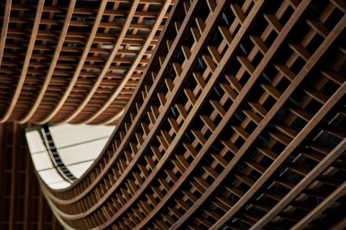 ZOZO: Close view of a curving wooden lattice ceiling with a gap of daylight between roof layers